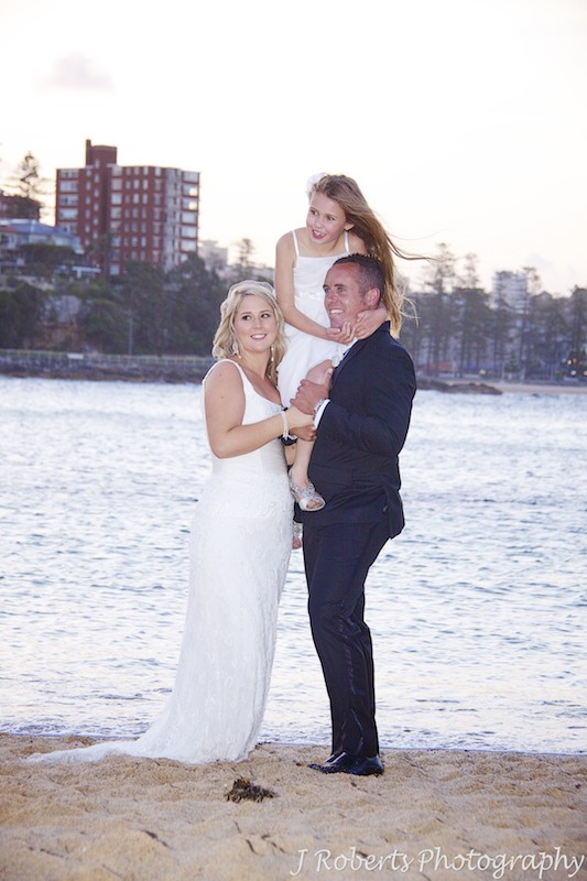 Groom holding daughter on shoulders and hugging bride - wedding photography sydney